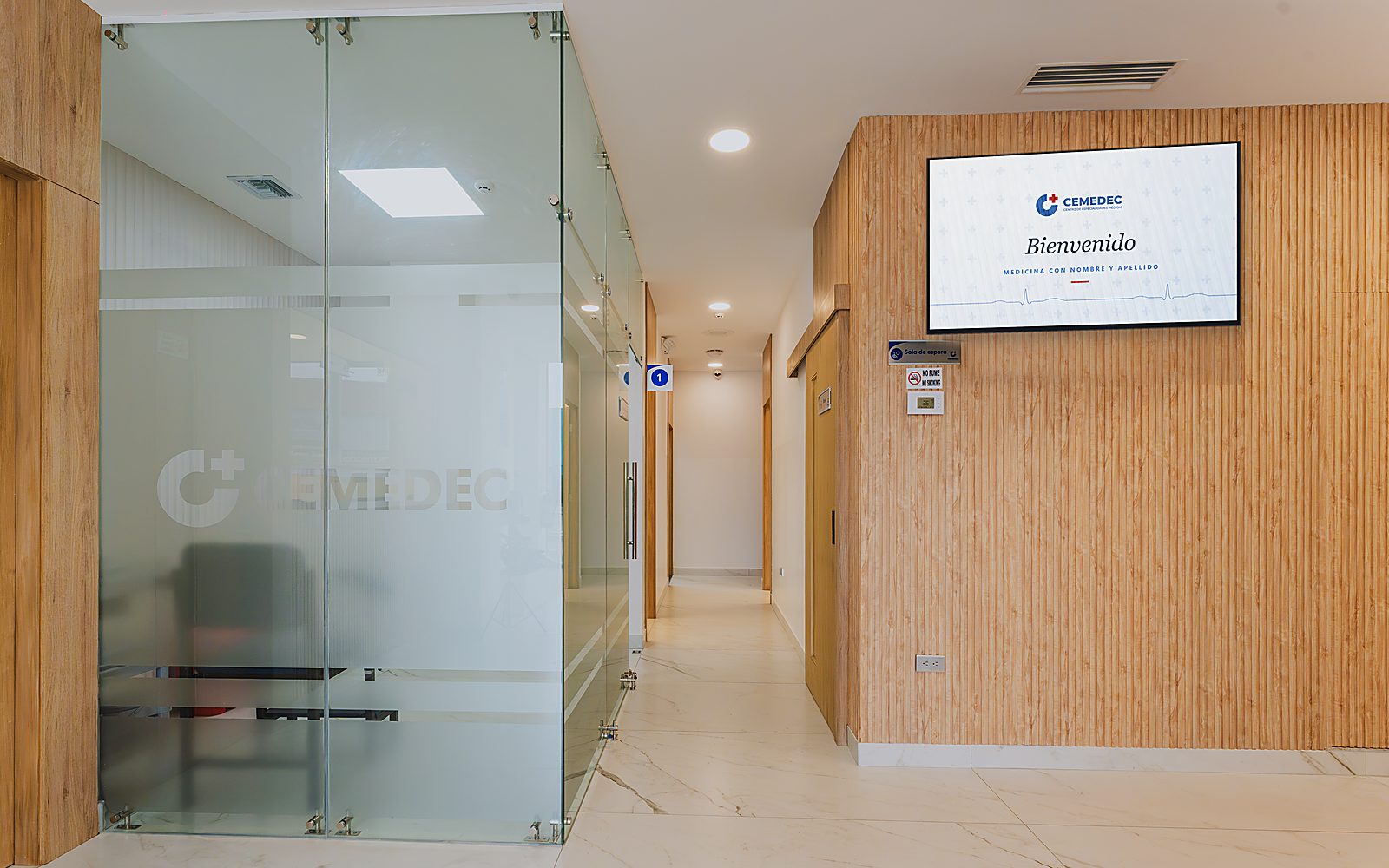 Pasillo de recepción de CEMEDEC, con el logotipo grabado en el vidrio y la pantalla de bienvenida que dice «Medicina con nombre y apellido»